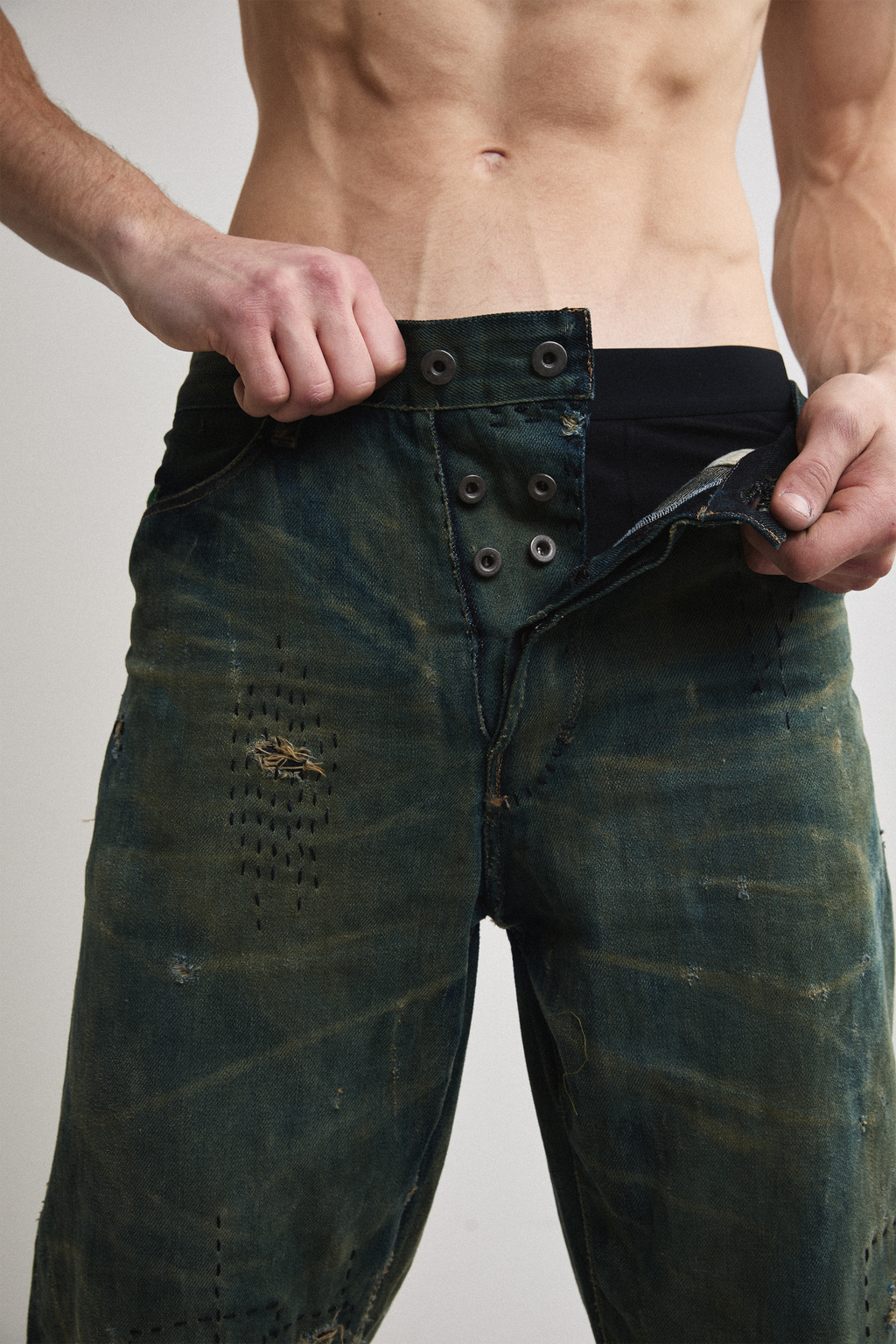 Close-up front view of Tyler Andersen wearing distressed AOA Sashiko repaired denim showing button fly