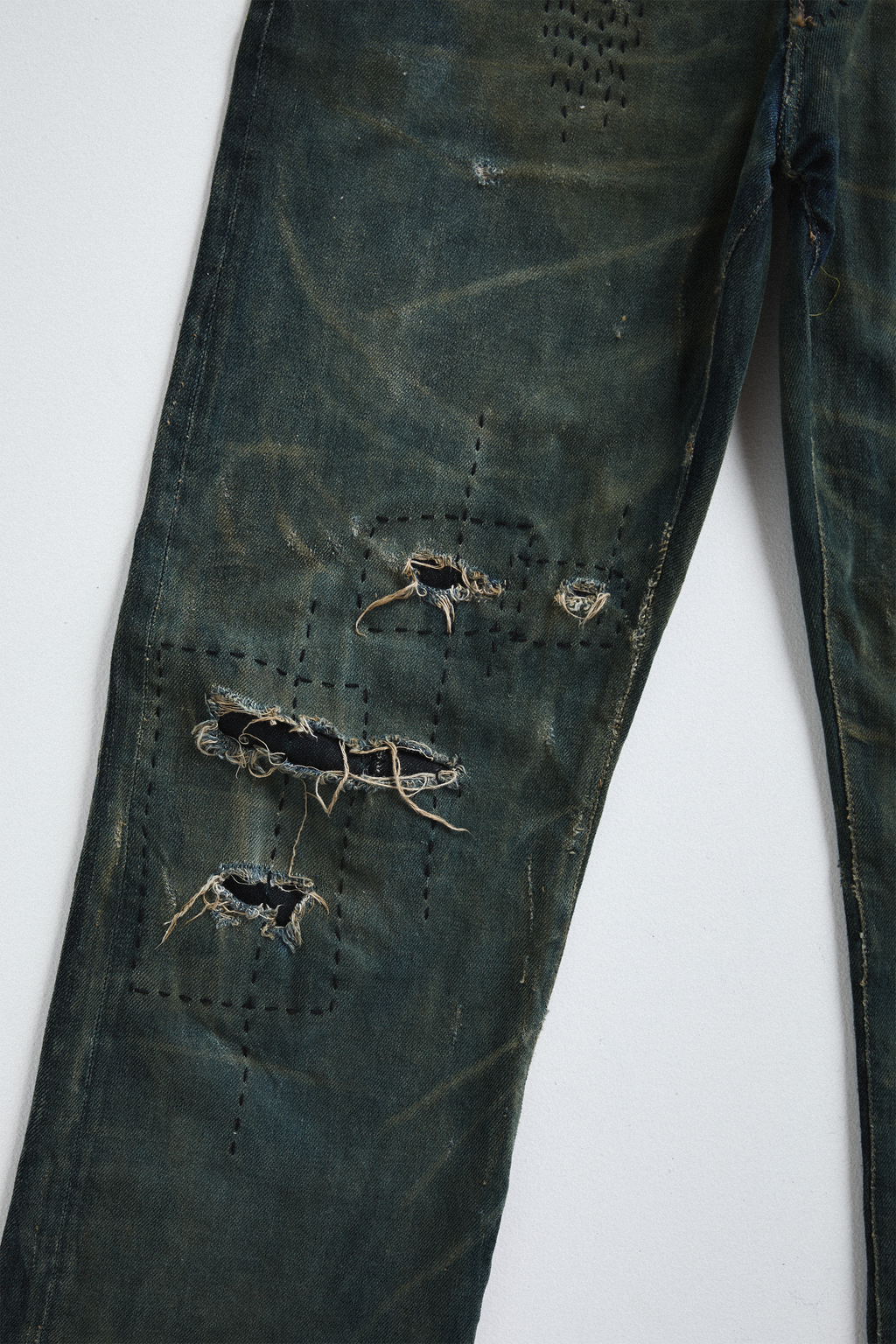 Ultra close-up front view of distressed AOA Sashiko repaired denim showing knee stitching details