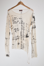 Front view of sheer long-sleeve AOA cream top with black text and graphics designed to look like tattoos.