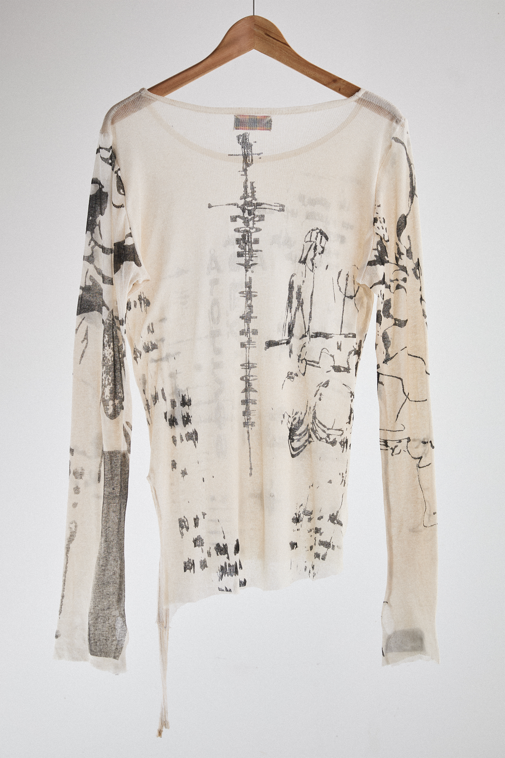 Back view of sheer long-sleeve cream AOA top with black text and graphics designed to look like tattoos.