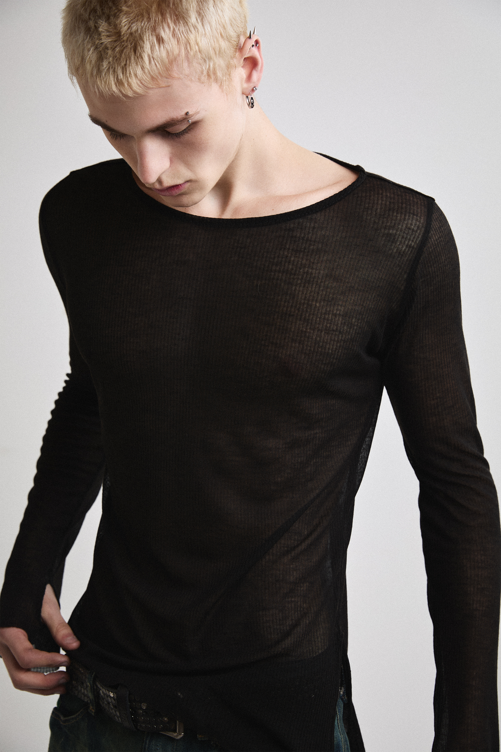 Close-up front view of Tyler Andersen looking down wearing sheer long-sleeve AOA Black top.