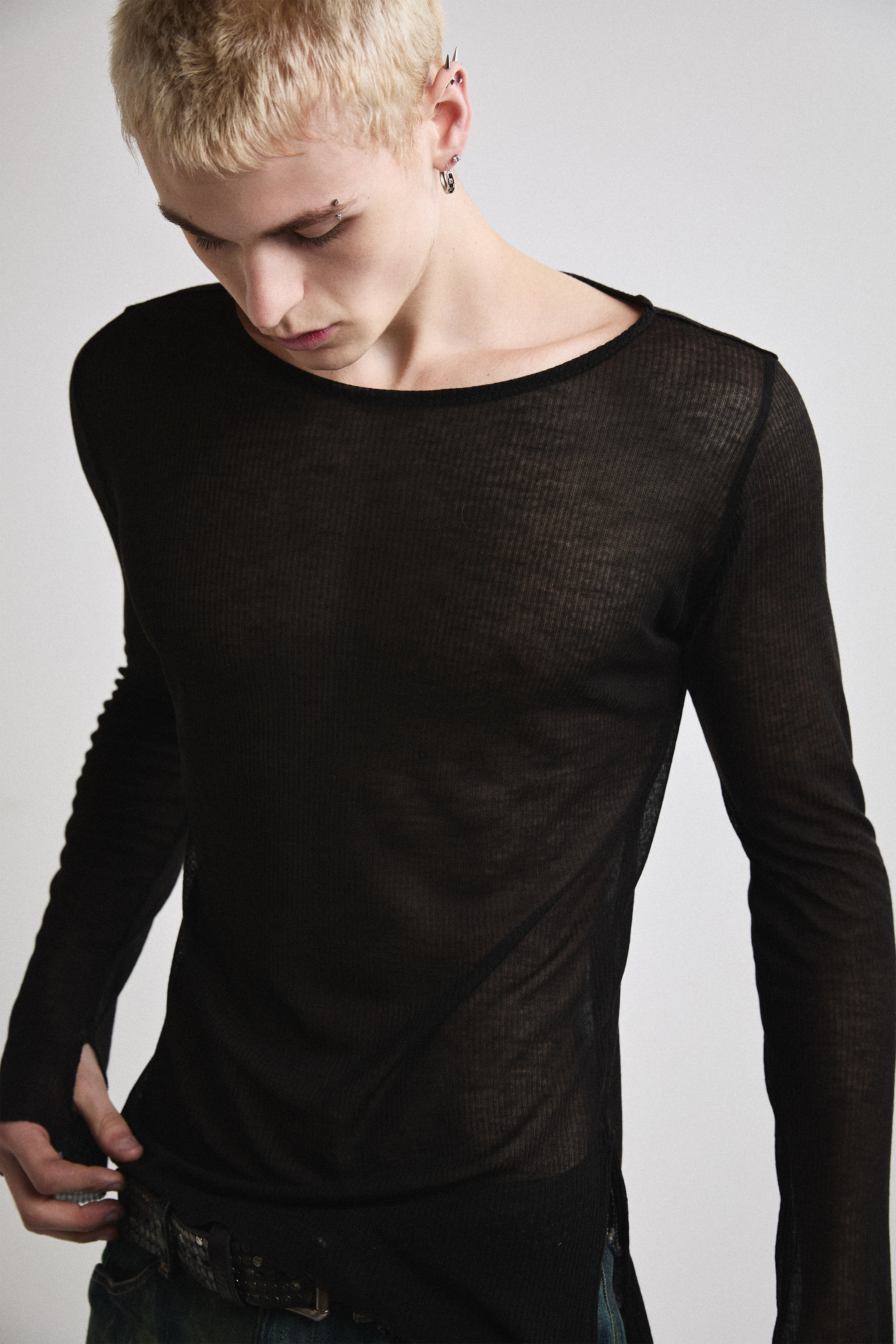 Close-up front view of Tyler Andersen looking down wearing sheer long-sleeve AOA Black top.