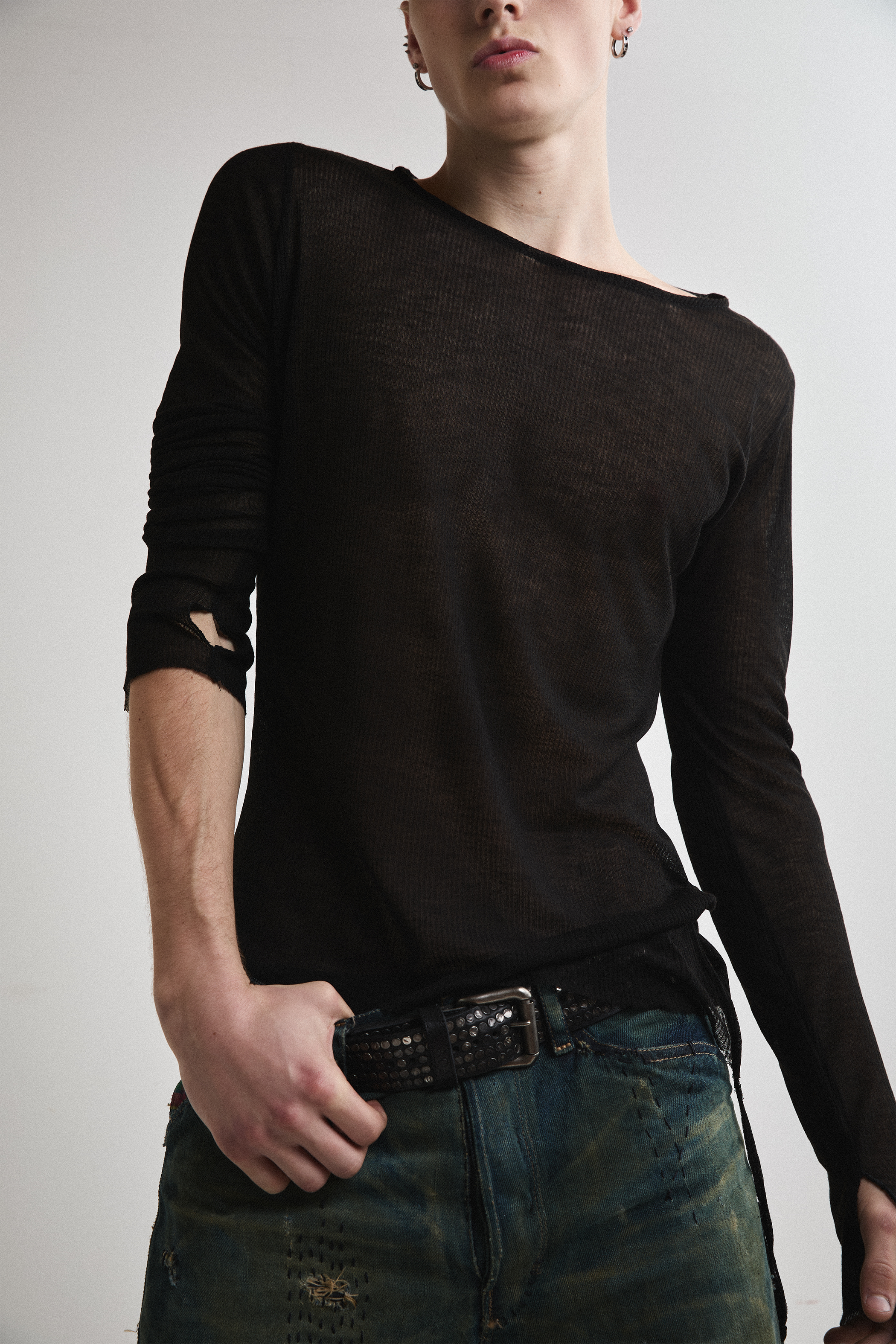 Close-up front view of Tyler Andersen with hand on belt wearing sheer long-sleeve AOA Black top.