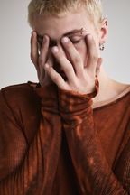 Close-up front view of Tyler Andersen  with hands on face wearing sheer long-sleeve AOA rust top.