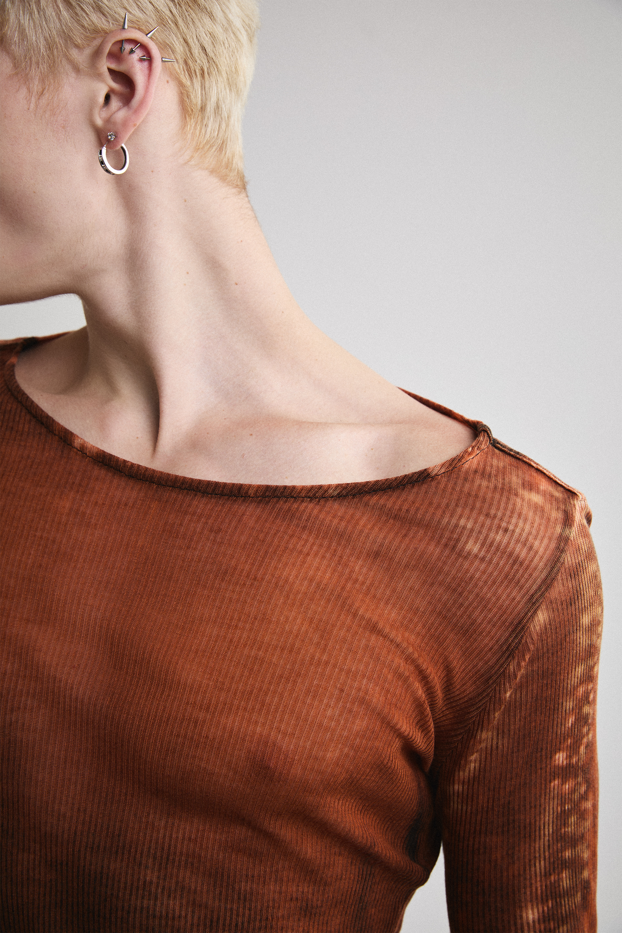 Ultra close-up view of Tyler Andersen looking left side view of Tyler Andersen wearing sheer long-sleeve AOA rust top.
