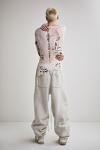 Back view of Tyler Andersen with hands showing wearing a sheer long-sleeve cream AOA top with black text and graphics designed to look like tattoos.