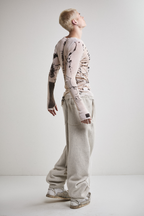 Side view of Tyler Andersen wearing a sheer long-sleeve cream AOA top with black text and graphics designed to look like tattoos.