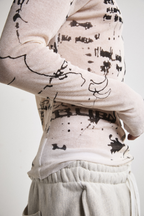Close-up right side view of Tyler Andersen wearing a sheer long-sleeve cream AOA top with black text and graphics designed to look like tattoos.
