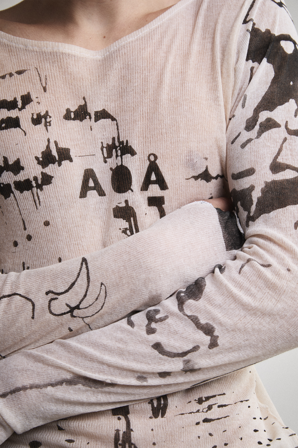 Ultra close-up view of Tyler Andersen wearing a sheer long-sleeve cream AOA top with black text and graphics designed to look like tattoos.