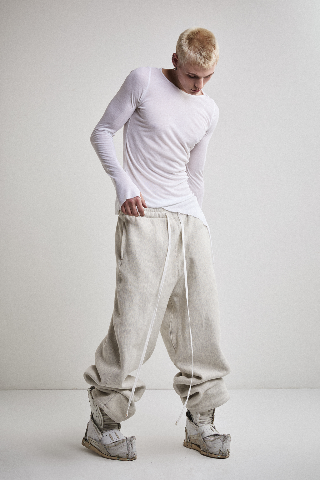 Front view of Tyler Andersen looking down wearing sheer long-sleeve AOA White  top.