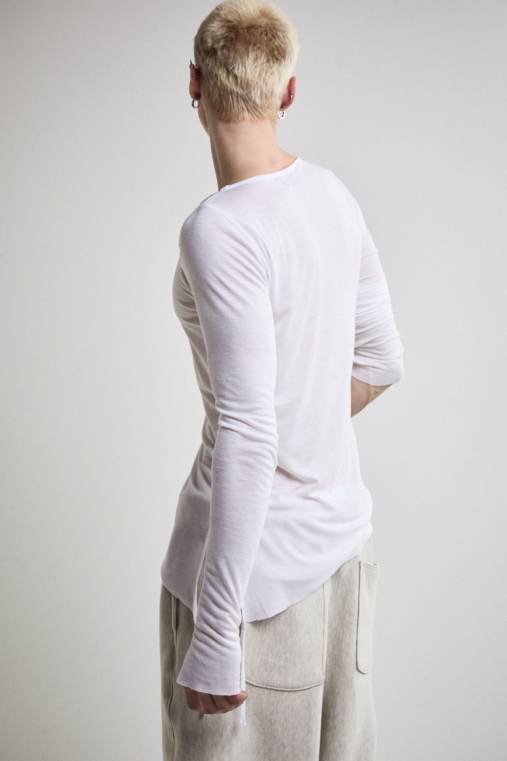 Close-up back view of Tyler Andersen wearing sheer long-sleeve AOA White  top.
