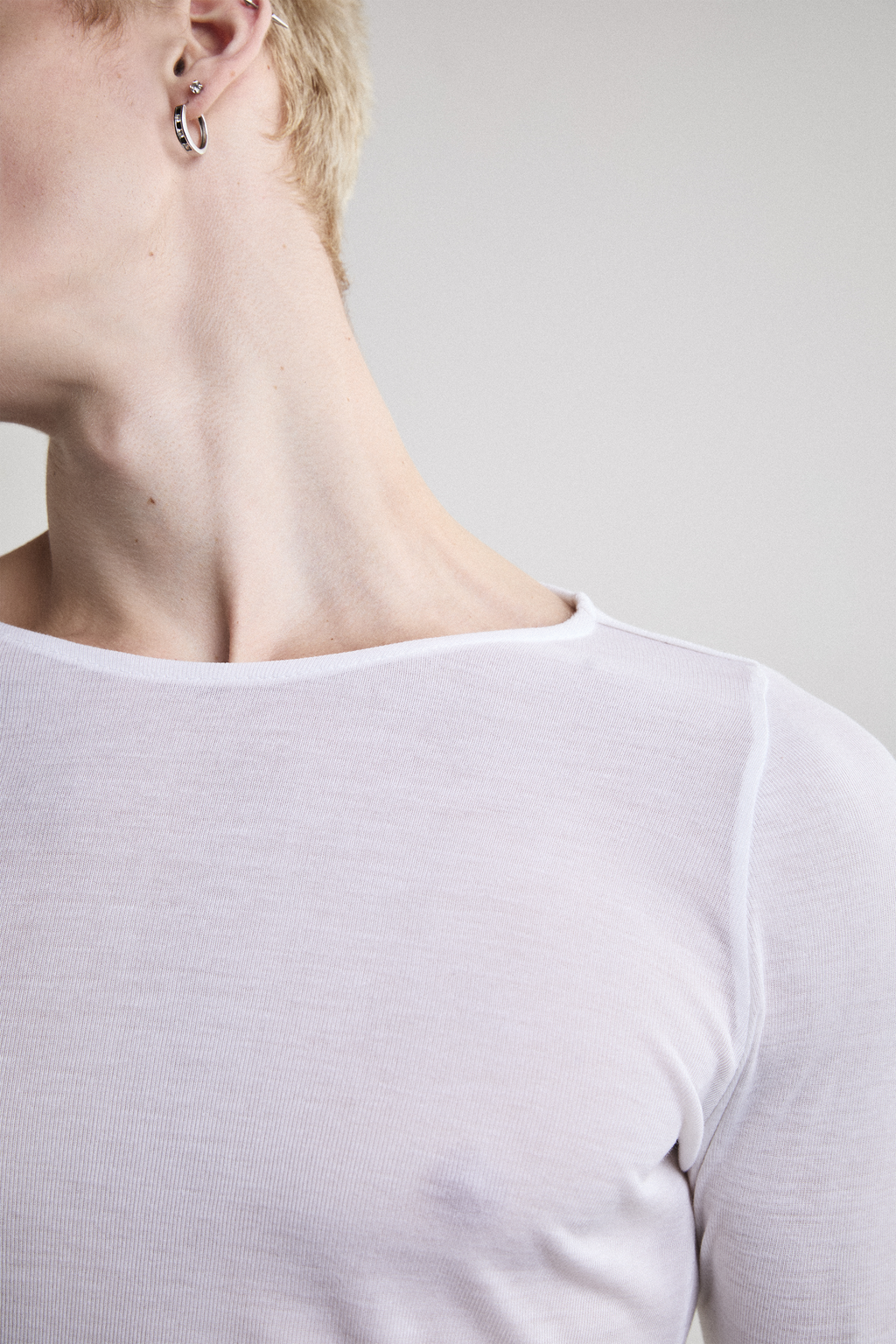 Ultra close-up front view of Tyler Andersen looking sideways wearing sheer long-sleeve AOA White  top.